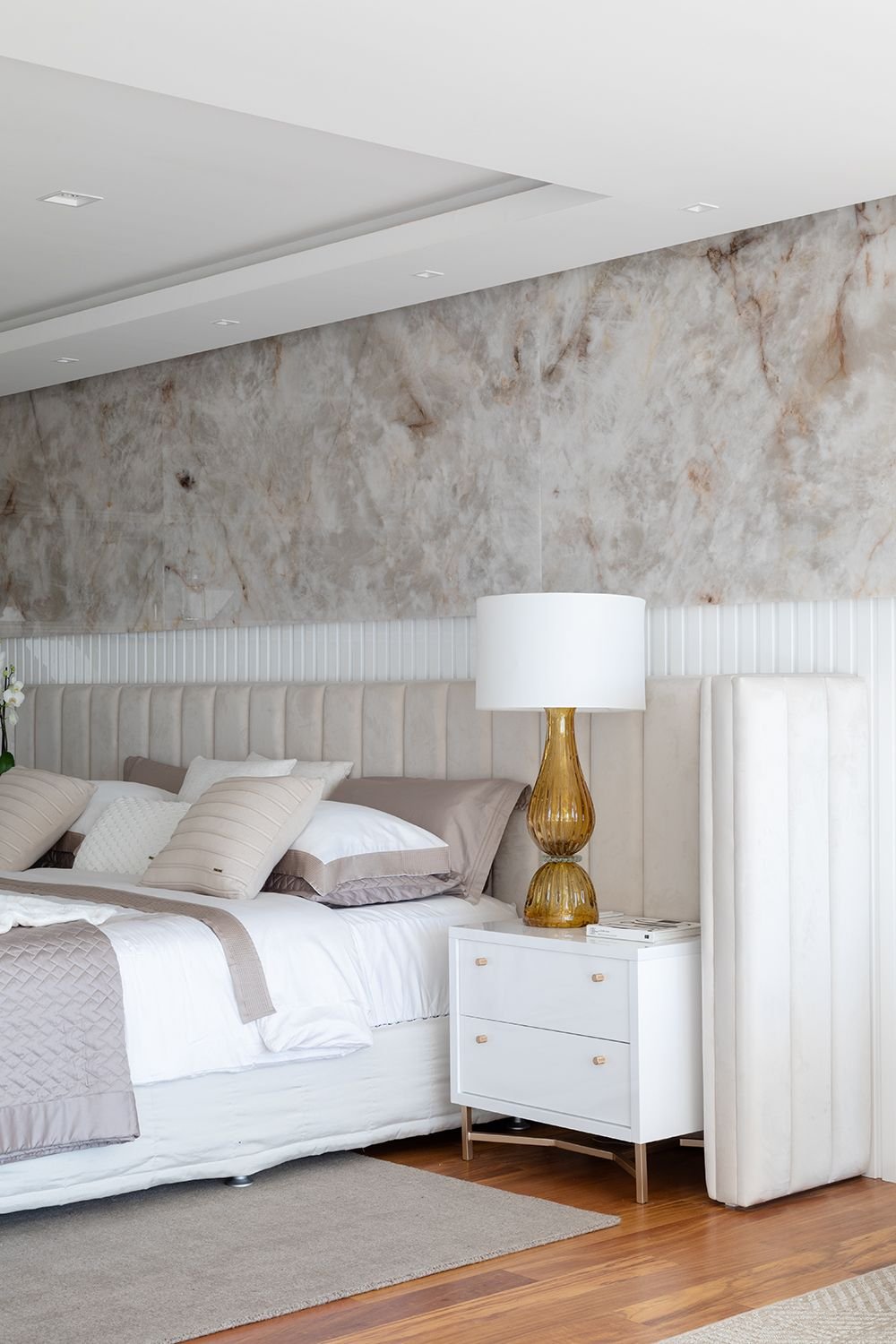Quarto claro com cabeceira estofada e parede em mármore