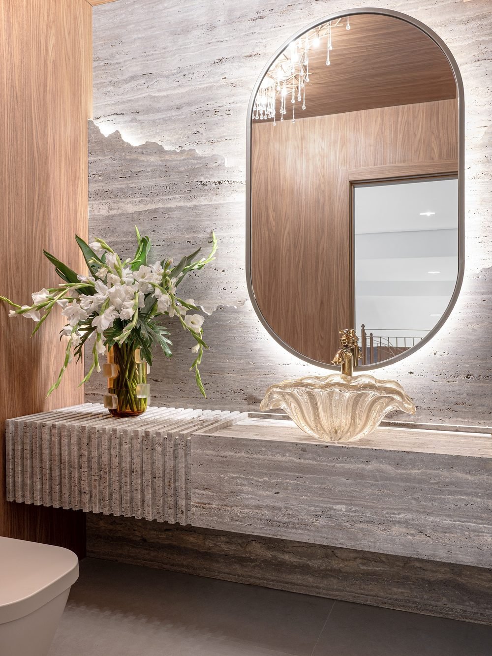 Lavabo com espelho oval iluminado e bancada em travertino