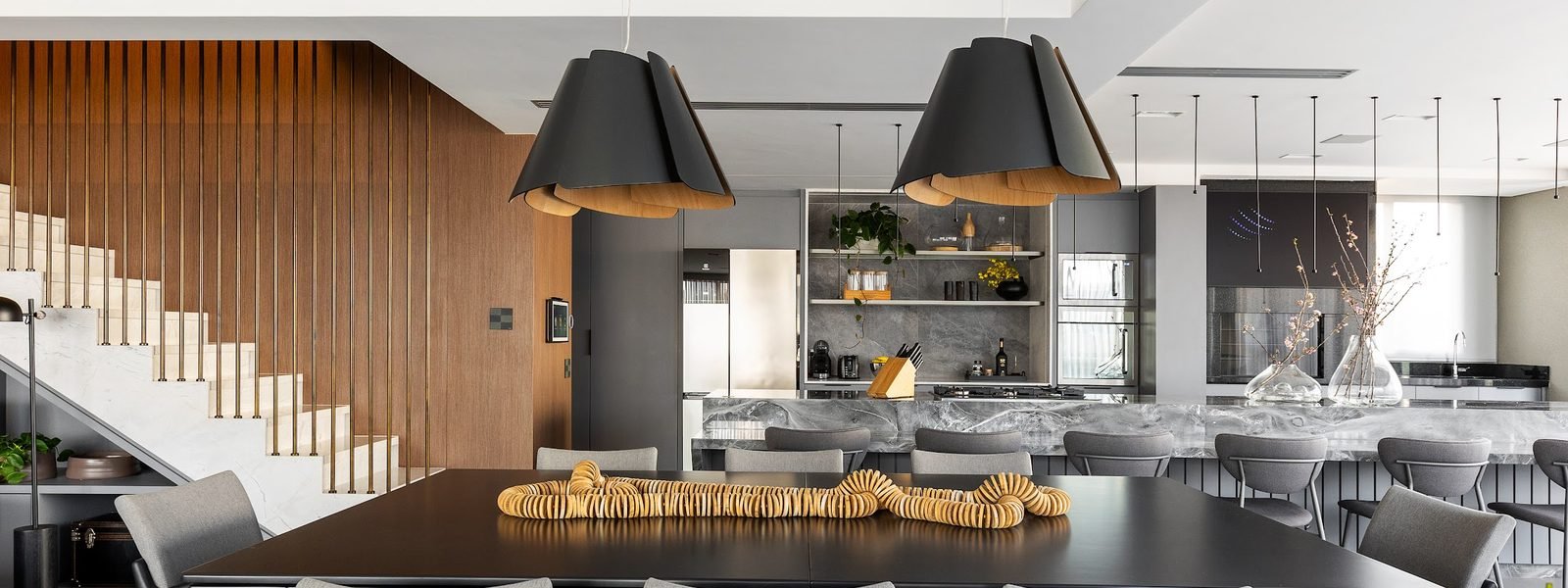 Sala de jantar integrada à cozinha, com mesa longa e pendentes pretos